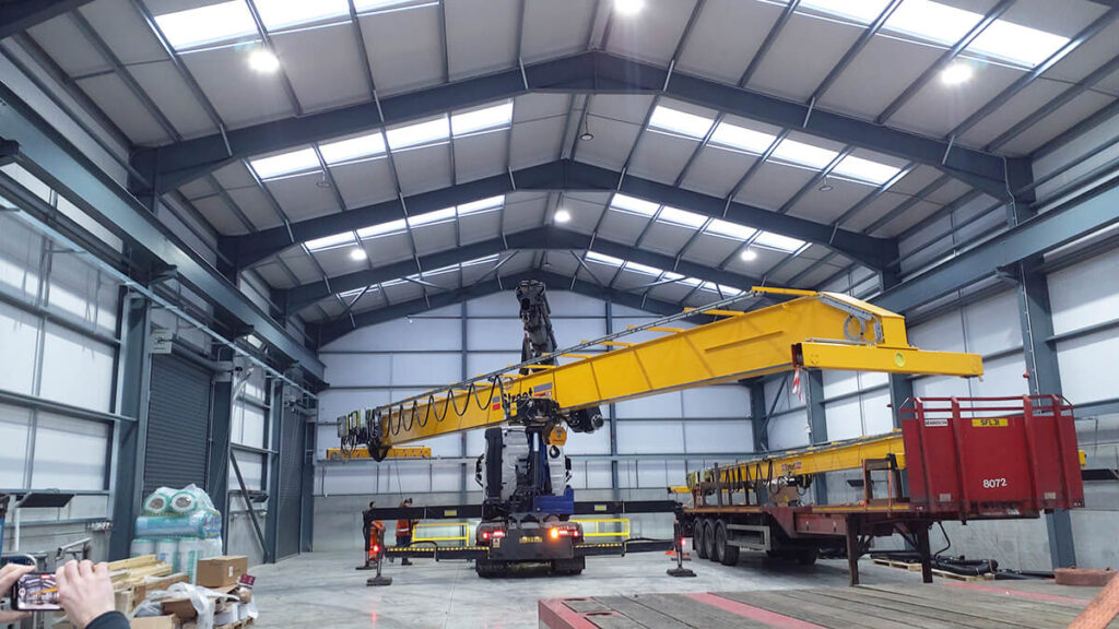Overhead crane being installed onto long travel rails using a HIAB truck in a new fabrication facility