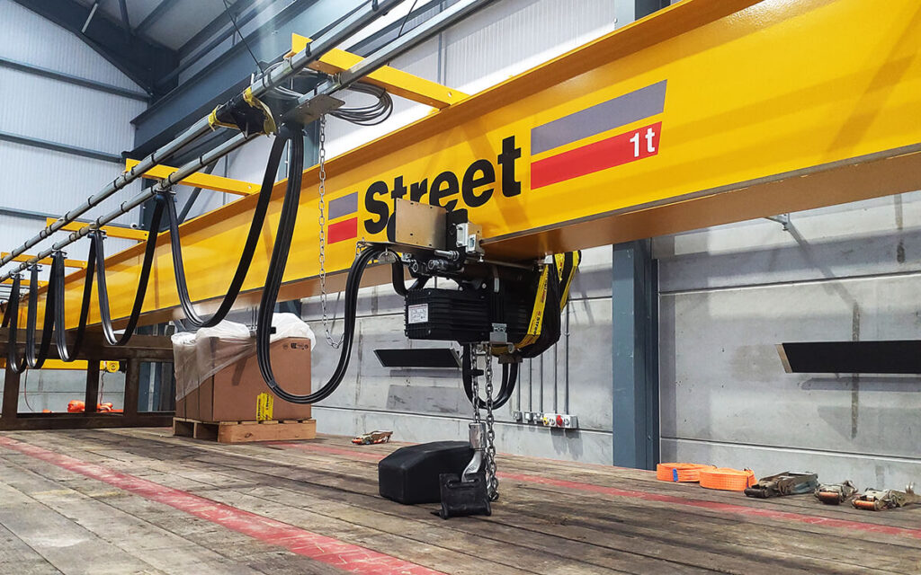Close-up of a single girder overhead crane showing the hoist and trolley system in a fabrication workshop.