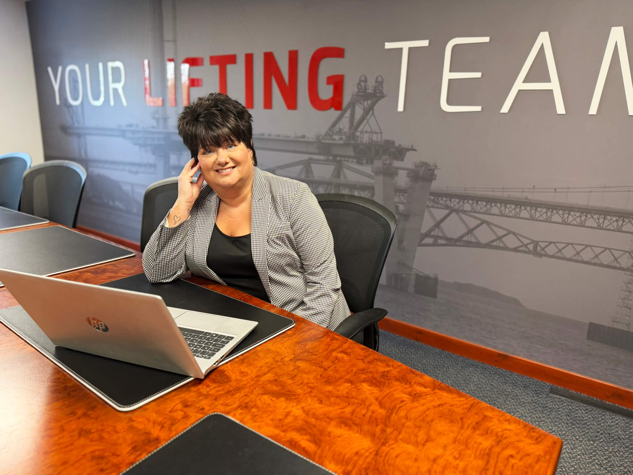 Person seated at a boardroom table with a laptop in front of branded wall graphics