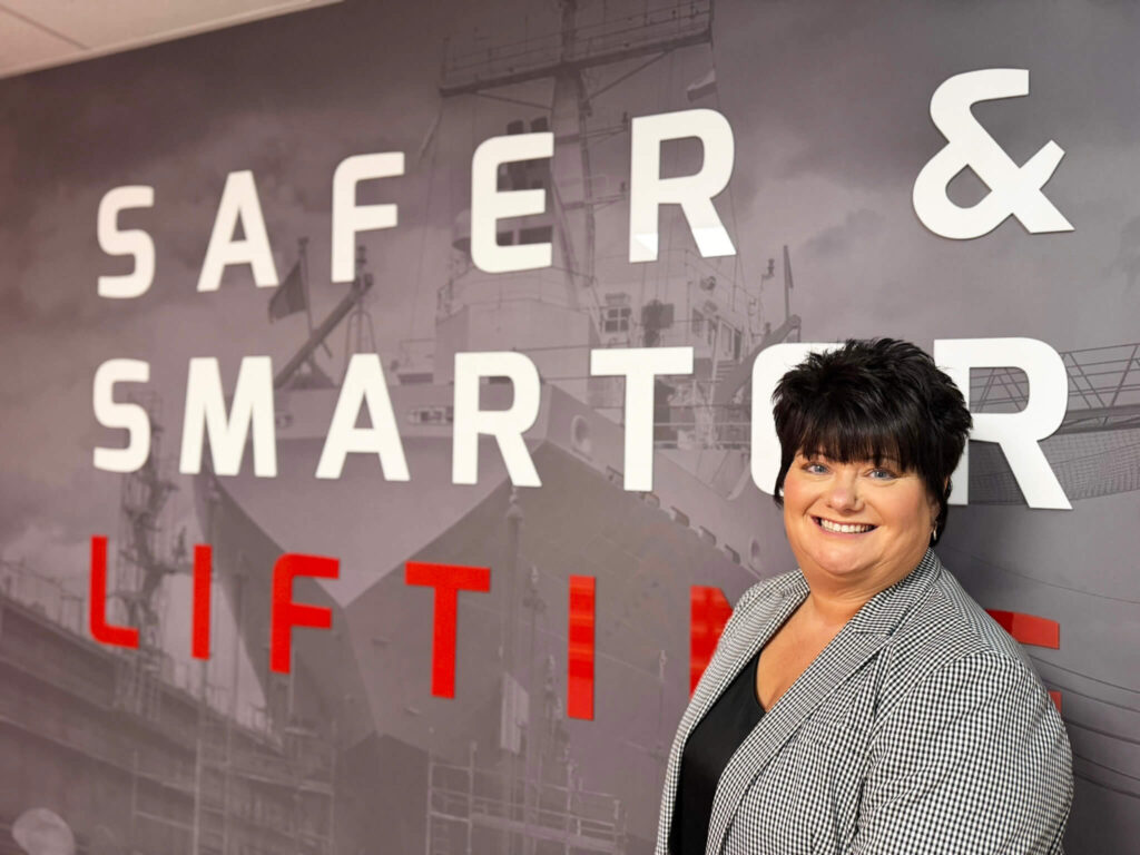 Person standing in front of a branded wall with the words “Safer & Smarter Lifting”
