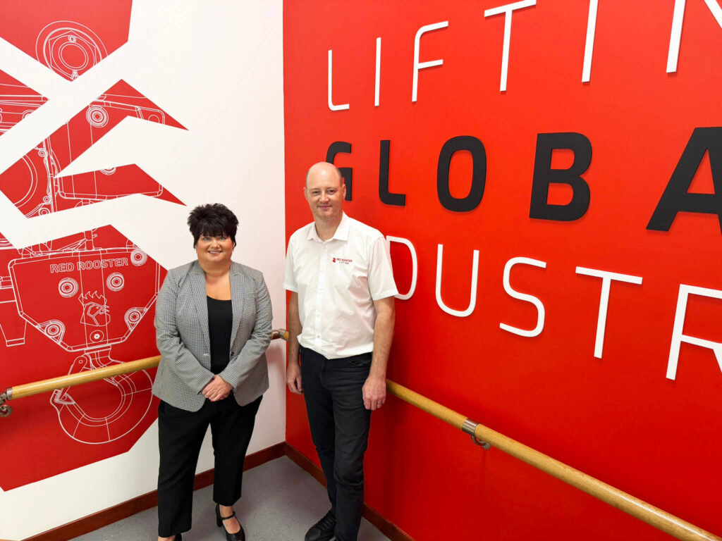 Two people standing on a stairwell in front of a branded red feature wall
