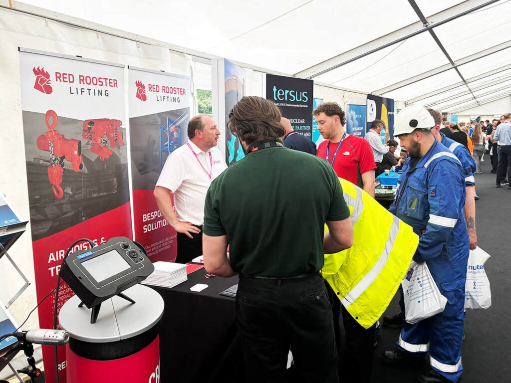 Red Rooster Lifting team members standing at a branded exhibition stand with product literature for air hoists and lifting solutions.