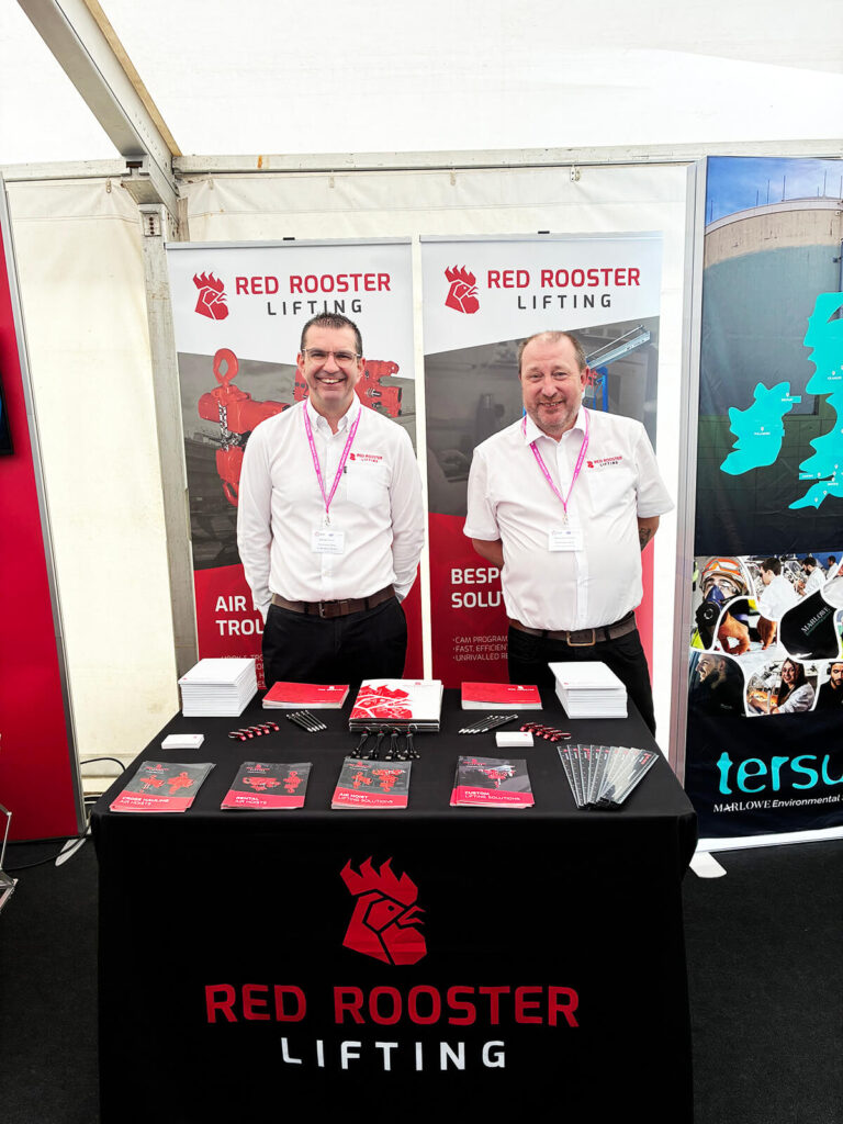 Red Rooster Lifting team members standing at a branded exhibition stand with product literature for air hoists and lifting solutions.